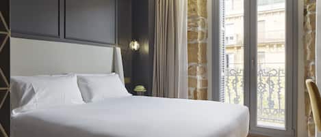 A hotel room with a large bed, a nightstand, a lamp, and a view of the outside balcony.