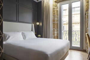 Habitación de hotel con una cama grande, una mesita de noche, una lámpara y vistas al balcón exterior.