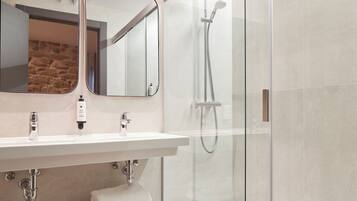 A modern bathroom with a glass shower enclosure, a white sink with a mirror above it, and a towel rack with folded towels.