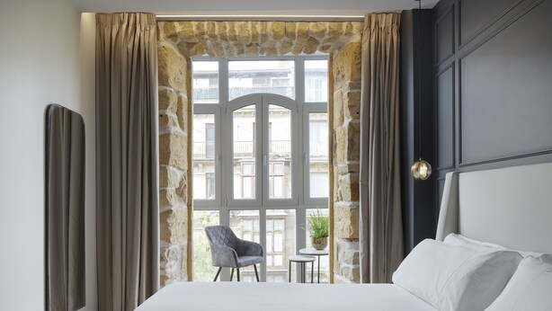 Habitación de hotel con una cama grande, una mesita con una silla y vistas al balcón exterior.