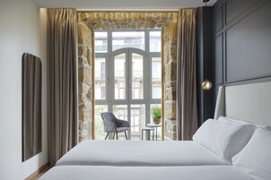 Habitación de hotel con una cama grande, una mesita con una silla y vistas al balcón exterior.