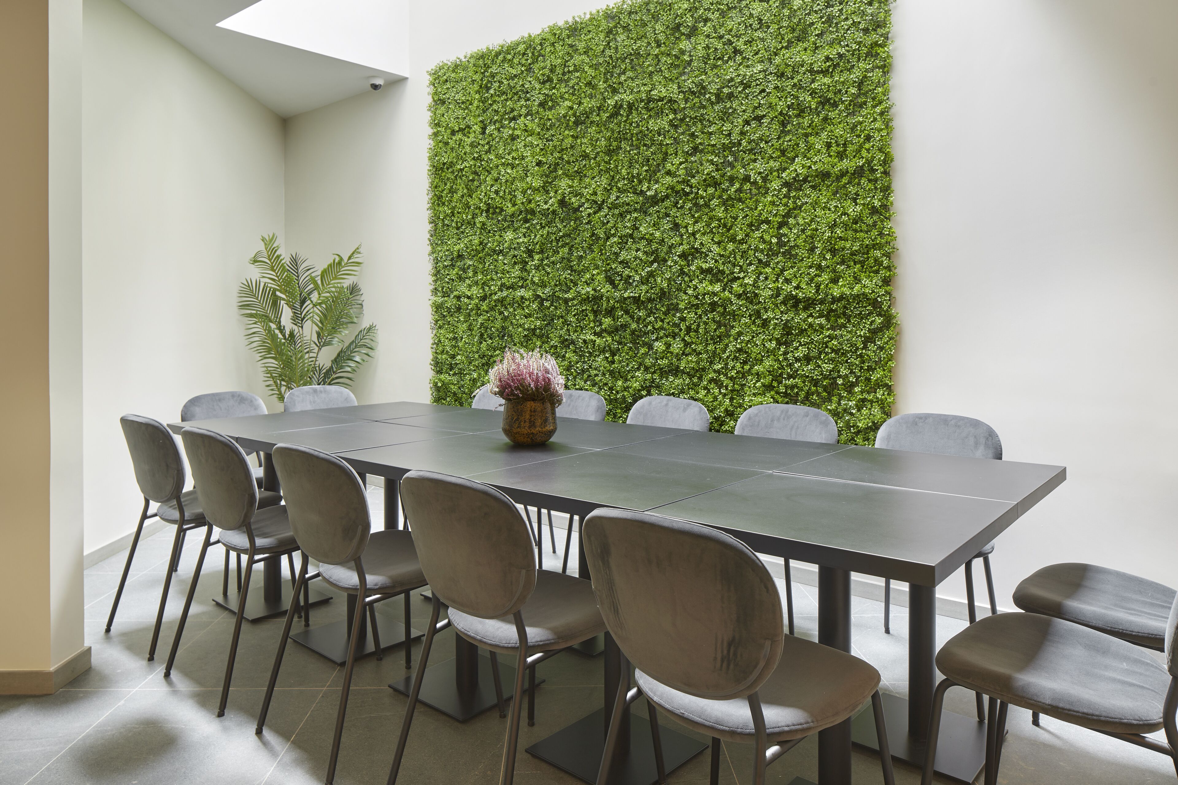 Une salle de conférence avec une longue table, six chaises et un mur végétal vertical.