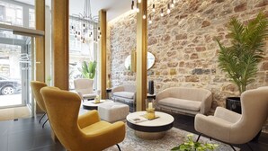 Un vestíbulo moderno con pared de piedra, sillas blancas y amarillas, una mesa de centro redonda y una gran planta en maceta.