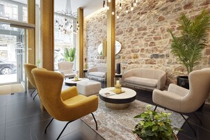 Un vestíbulo moderno con pared de piedra, sillas blancas y amarillas, una mesa de centro redonda y una gran planta en maceta.
