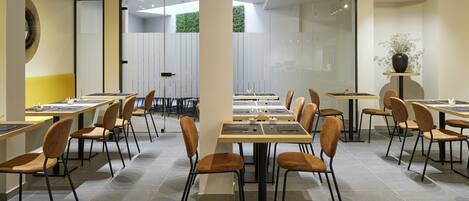 A modern dining area with multiple tables and chairs, glass partitions, and a potted plant.
