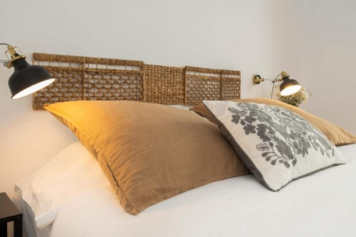 Una cama con dos almohadas, un cabecero con diseño trenzado y dos lámparas fijadas a la pared.