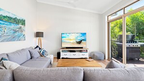 A modern living room with a grey sofa, a coffee table, a flat-screen TV, and a painting of a beach scene. - Bonito near Bagnalls Beach Corlette (Corlette)