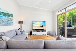 Een moderne woonkamer met een grijze bank, een salontafel, een flatscreen televisie en een schilderij van een strandgezicht.
