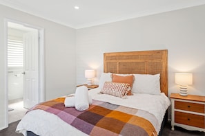 A bedroom with a bed, two bedside tables, a wooden headboard, and a door with blinds. - Bonito near Bagnalls Beach Corlette (Corlette)