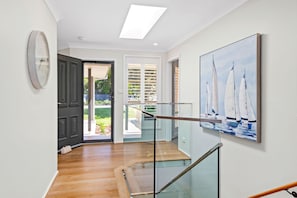 A modern interior with a staircase, a painting of sailboats, and a door leading to an outdoor area. - Bonito near Bagnalls Beach Corlette (Corlette)