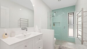 A modern bathroom with a white vanity, a glass shower enclosure, and a herringbone-patterned wall. - Bonito near Bagnalls Beach Corlette (Corlette)