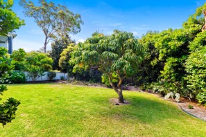 A well-maintained garden with a variety of trees and shrubs, a lawn, and a white fence. - Bonito near Bagnalls Beach Corlette (Corlette)