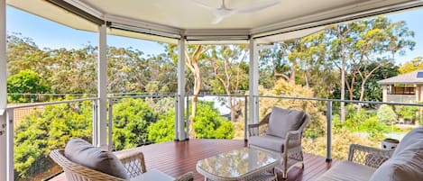 A covered outdoor area with wicker furniture, a glass table, and a ceiling fan.