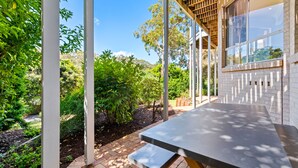 A covered outdoor area with a table and benches, surrounded by greenery and a brick wall. - Bonito near Bagnalls Beach Corlette (Corlette)