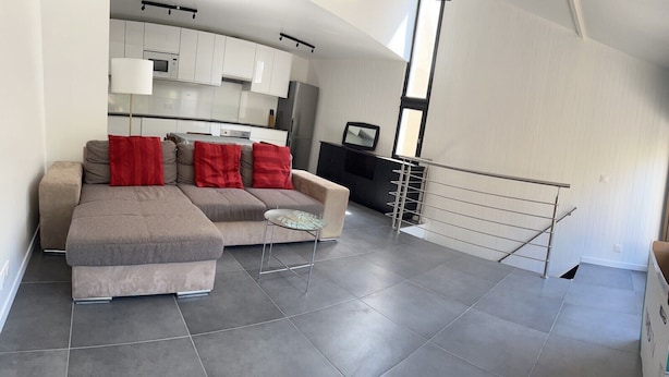 A modern living room with a sectional sofa, a small round table, and a built-in kitchen area. - Beautiful duplex with terrace and parking (Ivry-sur-Seine)