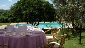 Un espacio de comedor al aire libre con una mesa dispuesta para cuatro personas, rodeado de sillas de mimbre, con vistas a una piscina.