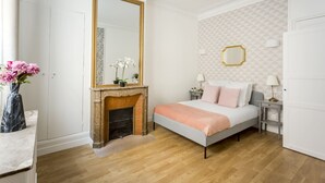 Un dormitorio con cama, chimenea, un espejo grande y un papel tapiz con diseño geométrico.