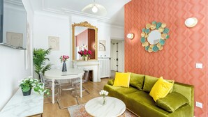 Una sala de estar moderna con un sofá verde, una mesa de centro redonda blanca y un comedor con una mesa y sillas blancas.