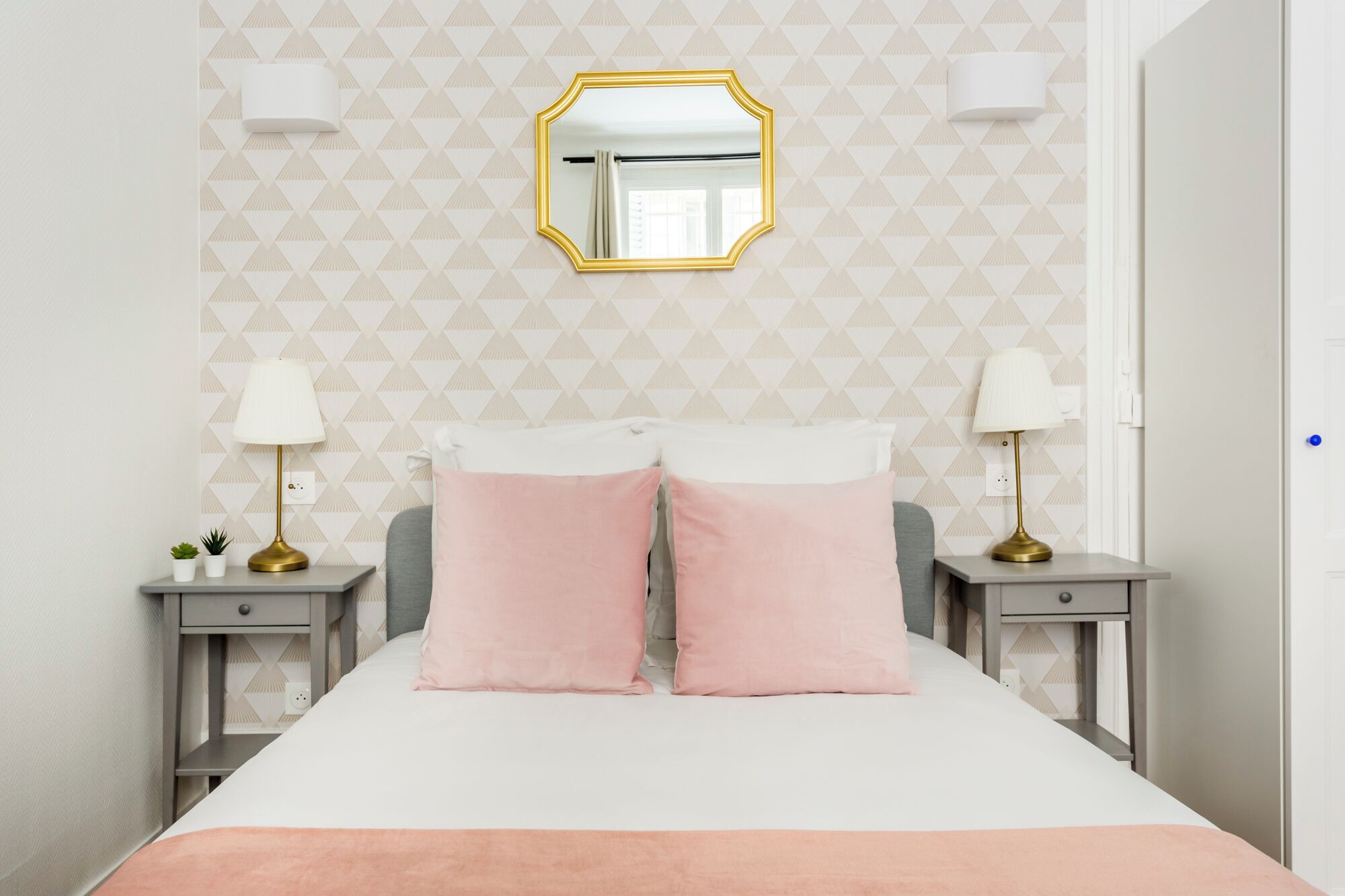 Een slaapkamer met een bed, twee nachtkastjes, een spiegel en een wand met een geometrisch patroon.