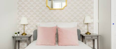 Een slaapkamer met een bed, twee nachtkastjes, een spiegel en een wand met een geometrisch patroon.
