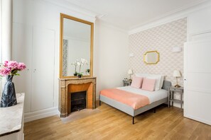 A bedroom with a bed, a fireplace, a large mirror, and a wall with geometric patterns. - Merveil - Family Suite - Opera - Cardinal Mercier (Paris)