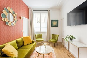 A modern living room with a green sofa, two green armchairs, a round coffee table, and a decorative mirror. - Merveil - Family Suite - Opera - Cardinal Mercier (Paris)