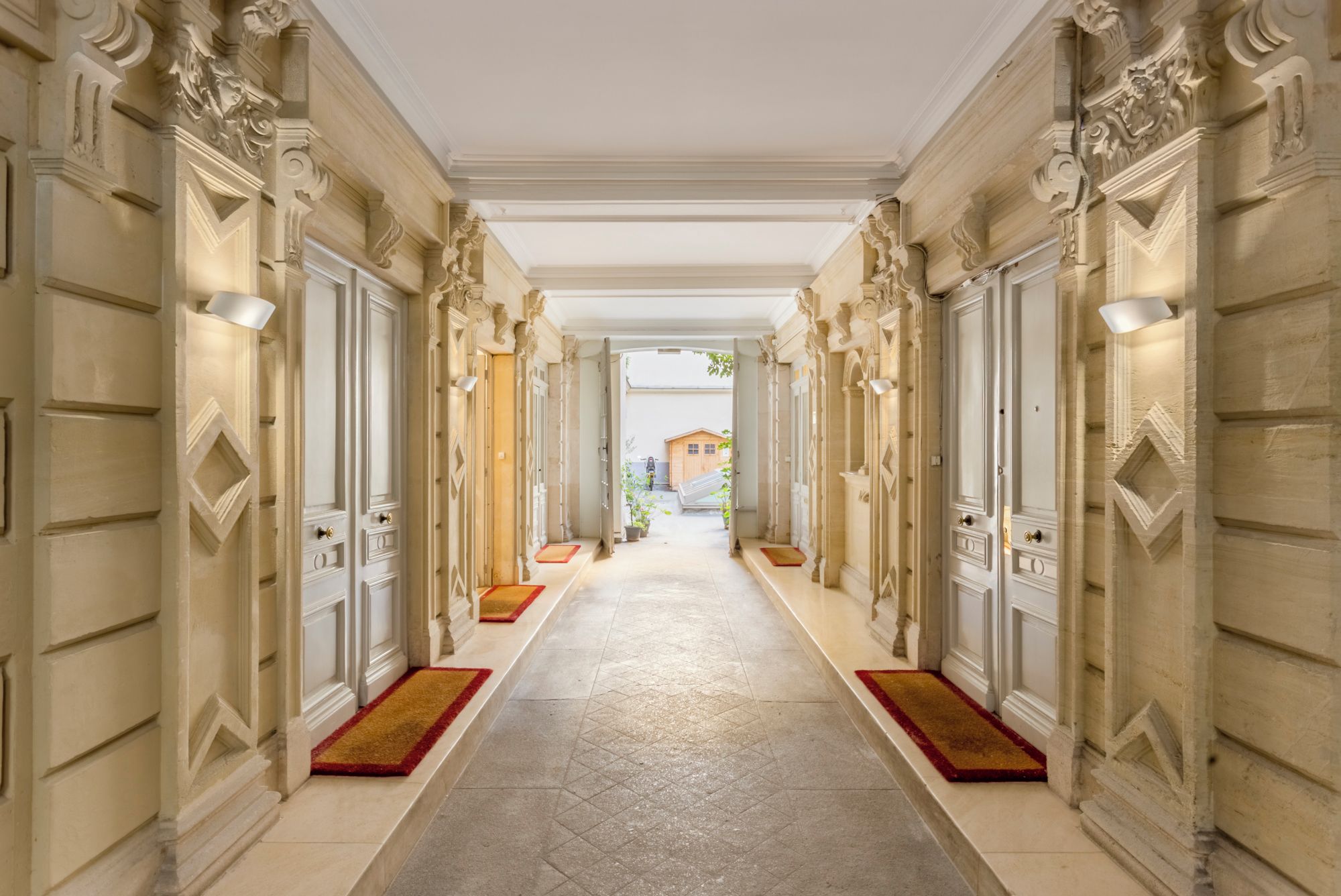 Un vaste hall d’entrée, orné de colonnes et de portes richement décorées, qui mène à une cour intérieure abritant une structure en bois.