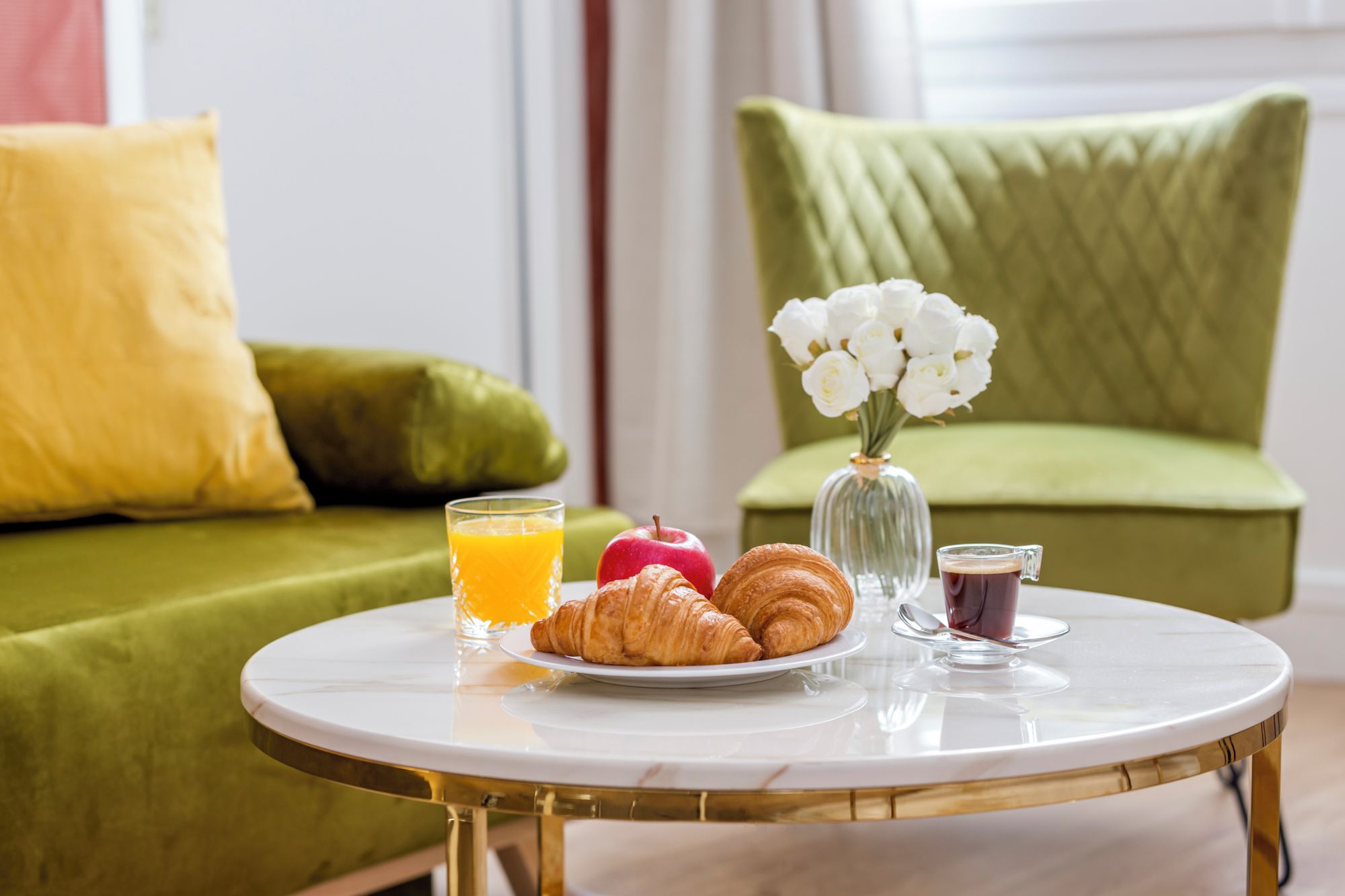 Une table ronde dressée pour le petit-déjeuner, avec des croissants, un verre de jus d’orange et une tasse de café.