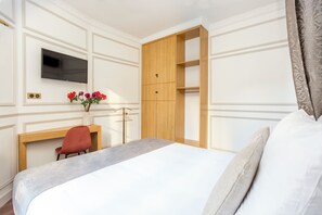 Een hotelkamer met een bed, een bureau, een televisie, een kledingkast en een bloemenvaas.