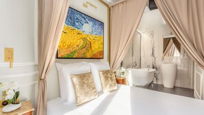 Un dormitorio con cama, un cuadro y un baño visible a través de una cortina.