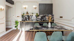Una cocina moderna con encimeras de mármol, un salpicadero negro y detalles dorados. Hay una mesa de comedor con sillas y un ventanal amplio arriba.