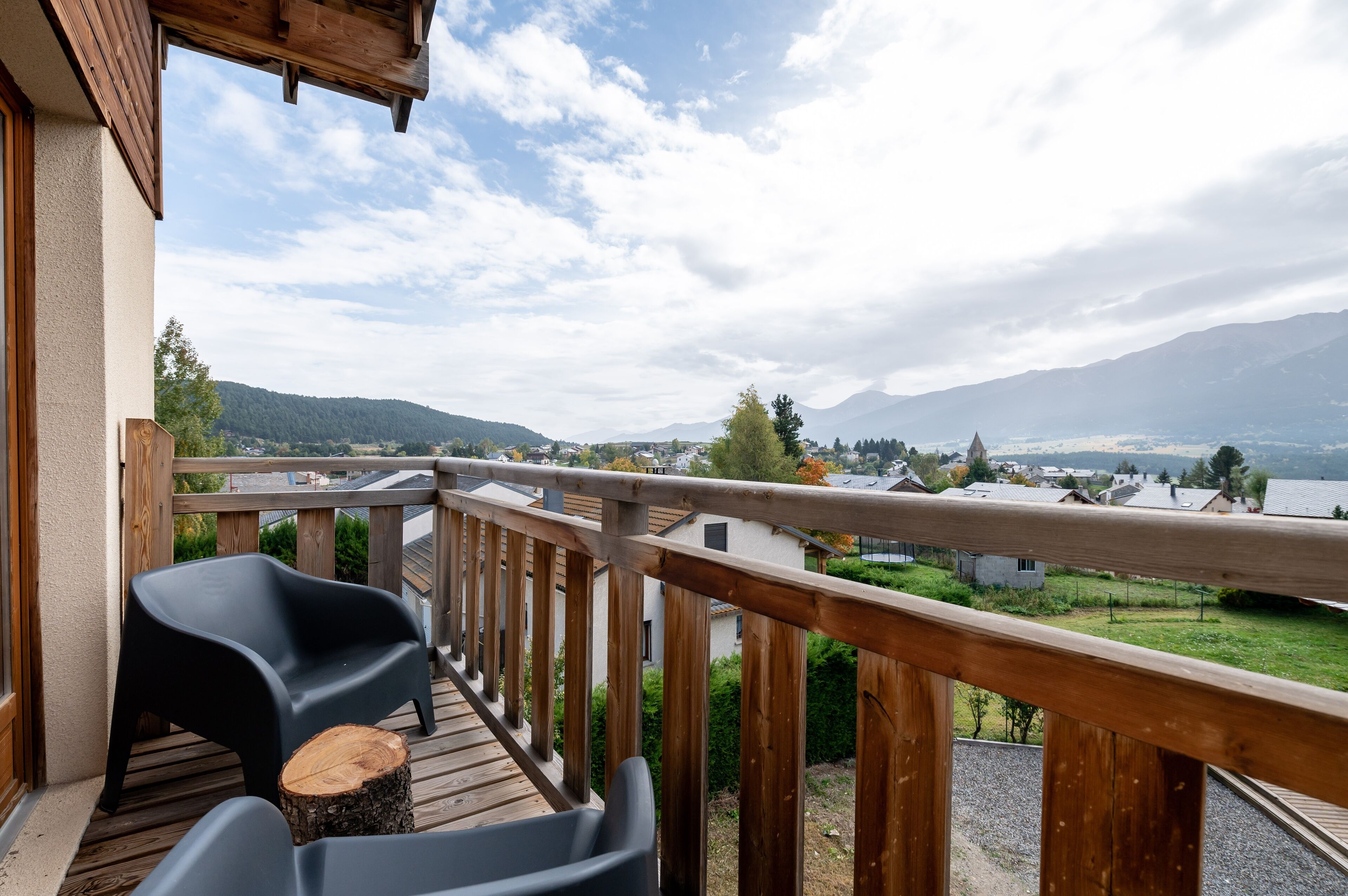 A wooden deck with a railing, two black chairs, and a wooden stump.