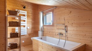 Un baño de cabaña de madera con una bañera blanca, repisas con cestas tejidas y una ventana con vistas.