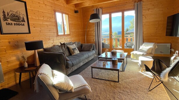 Interior acogedor de una cabaña de madera con sofá, sillón, mesa de centro y televisor.