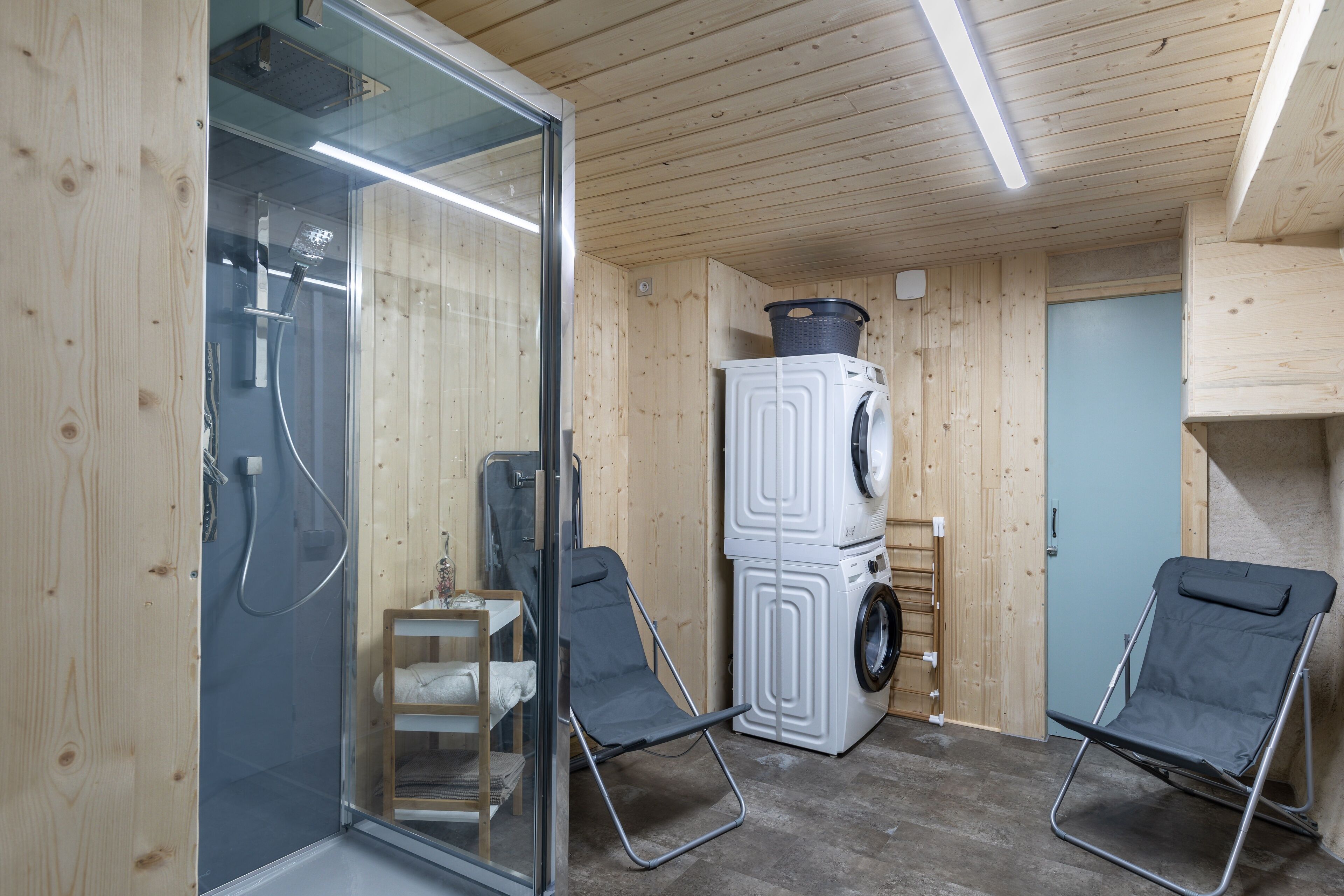 A compact room with a glass shower enclosure, a washing machine, and two foldable chairs.