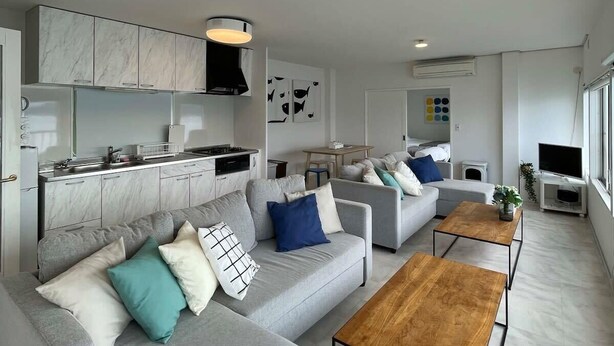A modern living room with a grey sofa set, a wooden coffee table, and a kitchen area with marble cabinets. - House with Ocean view good for 8PPL Free WiFi (Suooshima, Oshima District)