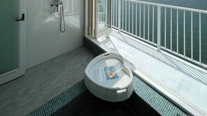 A modern bathroom with a glass-enclosed shower, a small round bathtub, and a view of a body of water and distant mountains.