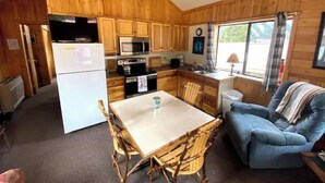 A compact kitchen with wooden cabinets, a microwave, stove, and a refrigerator. There's a dining table with chairs and a blue couch in the living area. - Eagle Nest Cabin Yellowstone Getaway in Cooke City (Cooke city)