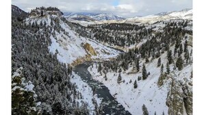 A snow-covered valley with a river, dense forests, and distant mountains.