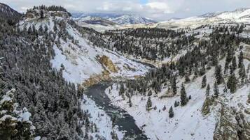 A snow-covered valley with a river, dense forests, and distant mountains.