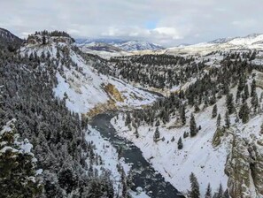Un vall format de neu, un riu, boscos densos i muntanyes allunyades.