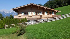 A wooden chalet with a balcony, set against a backdrop of mountains and a clear sky. - Kitz-Chalet - Luxury Chalet in Kitzbühel (Kitzbühel)