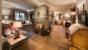 A cozy living room with a fireplace, a sofa, a coffee table, and a lamp. - Kitz-Chalet - Luxury Chalet in Kitzbühel (Kitzbühel)