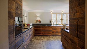 A modern kitchen with wooden cabinetry, a black countertop, and a window providing natural light. - Kitz-Chalet - Luxury Chalet in Kitzbühel (Kitzbühel)