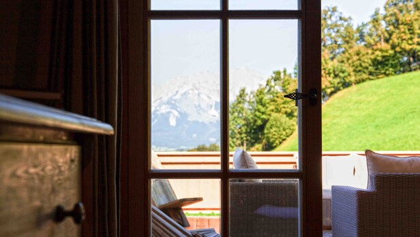 A view from a room with a wooden door leading to an outdoor deck with wicker furniture and a mountain backdrop. - Kitz-Chalet - Luxury Chalet in Kitzbühel (Kitzbühel)