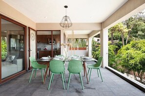 A dining area with a glass table and chairs, a hanging light fixture, and a view of greenery. - Villa del Lago: Overlooking the lake in Avándaro (Valle de Bravo)