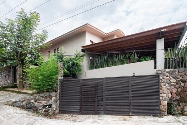 A modern house with a stone wall, metal gates, and a covered patio area.
