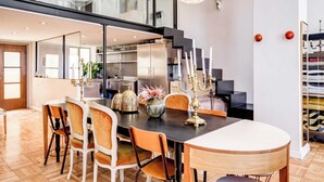 A modern dining area with a glass staircase, a chandelier, and a view of the kitchen.