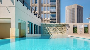 A swimming pool with a stone wall and a staircase leading to a balcony.