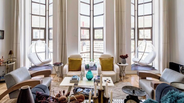 A spacious living room with large windows, a hanging chair, a coffee table, and a sofa.